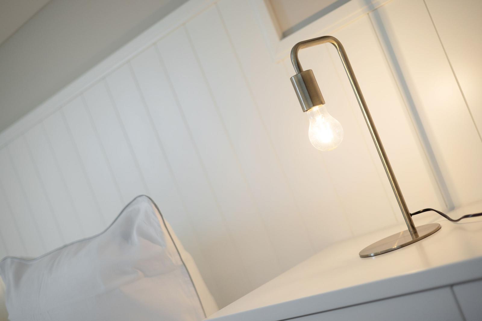 Eine Lampe mit Glühbirne steht auf einem Nachttisch neben einem Kissen.
