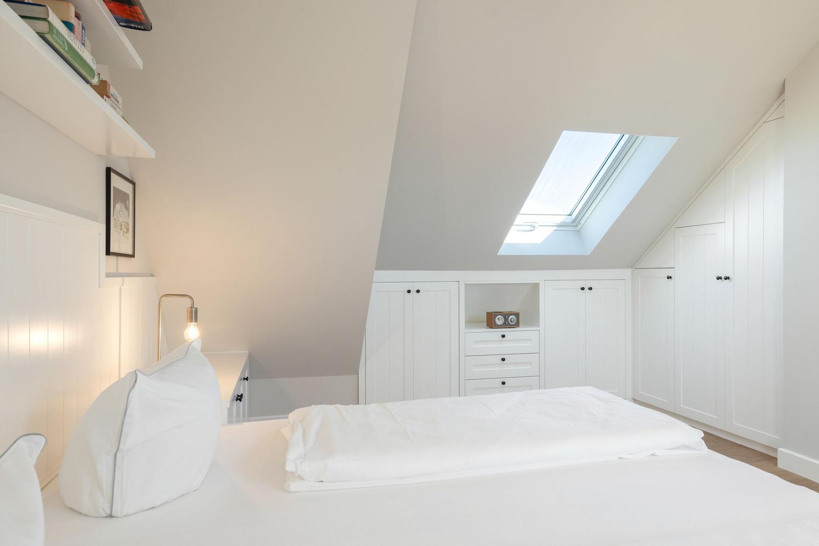 Schlafzimmer mit Dachfenster, weißem Bett und Schränken.
