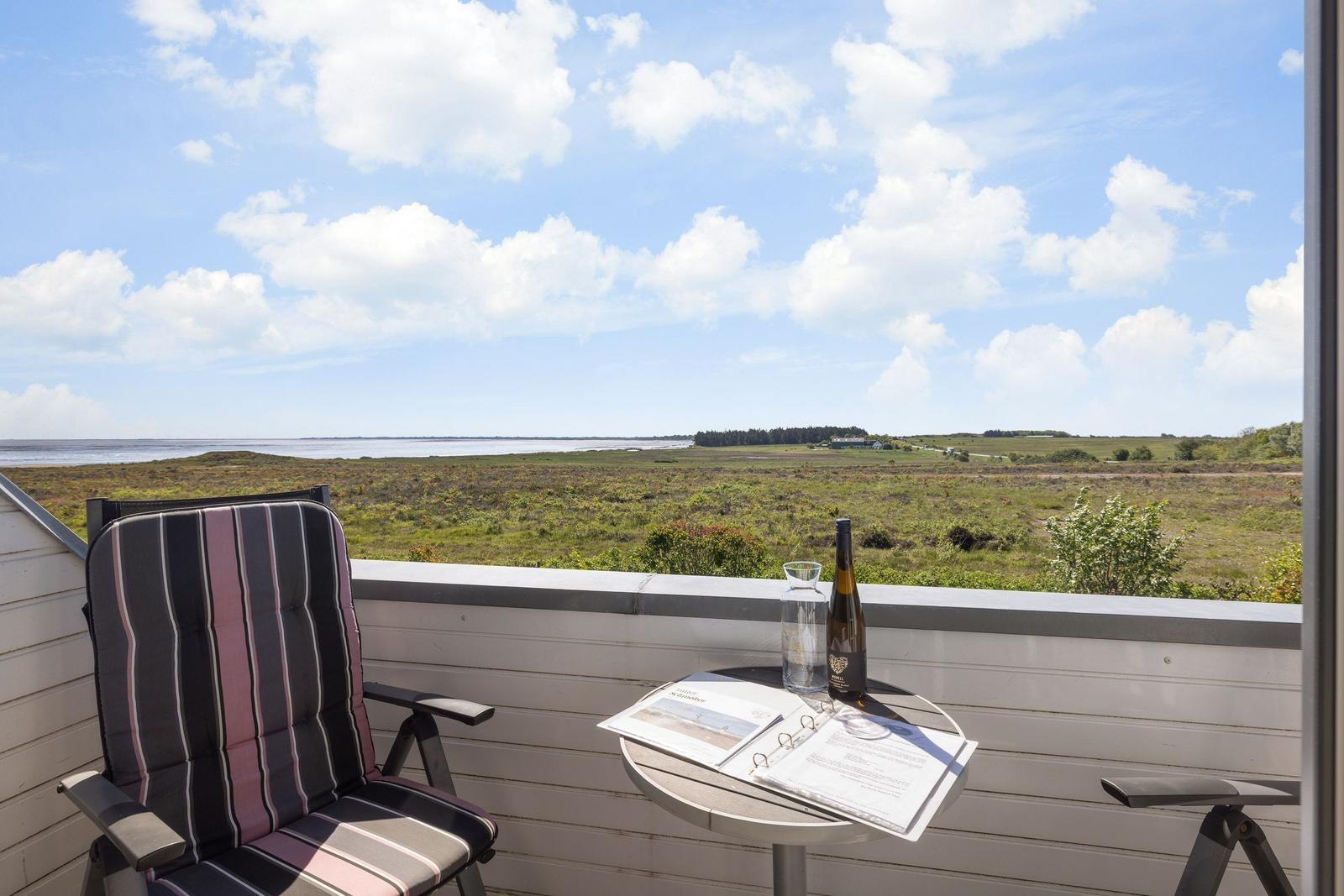 Terrasse mit Stuhl und Tisch. Blick auf Feld und Wasser unter blauem Himmel.