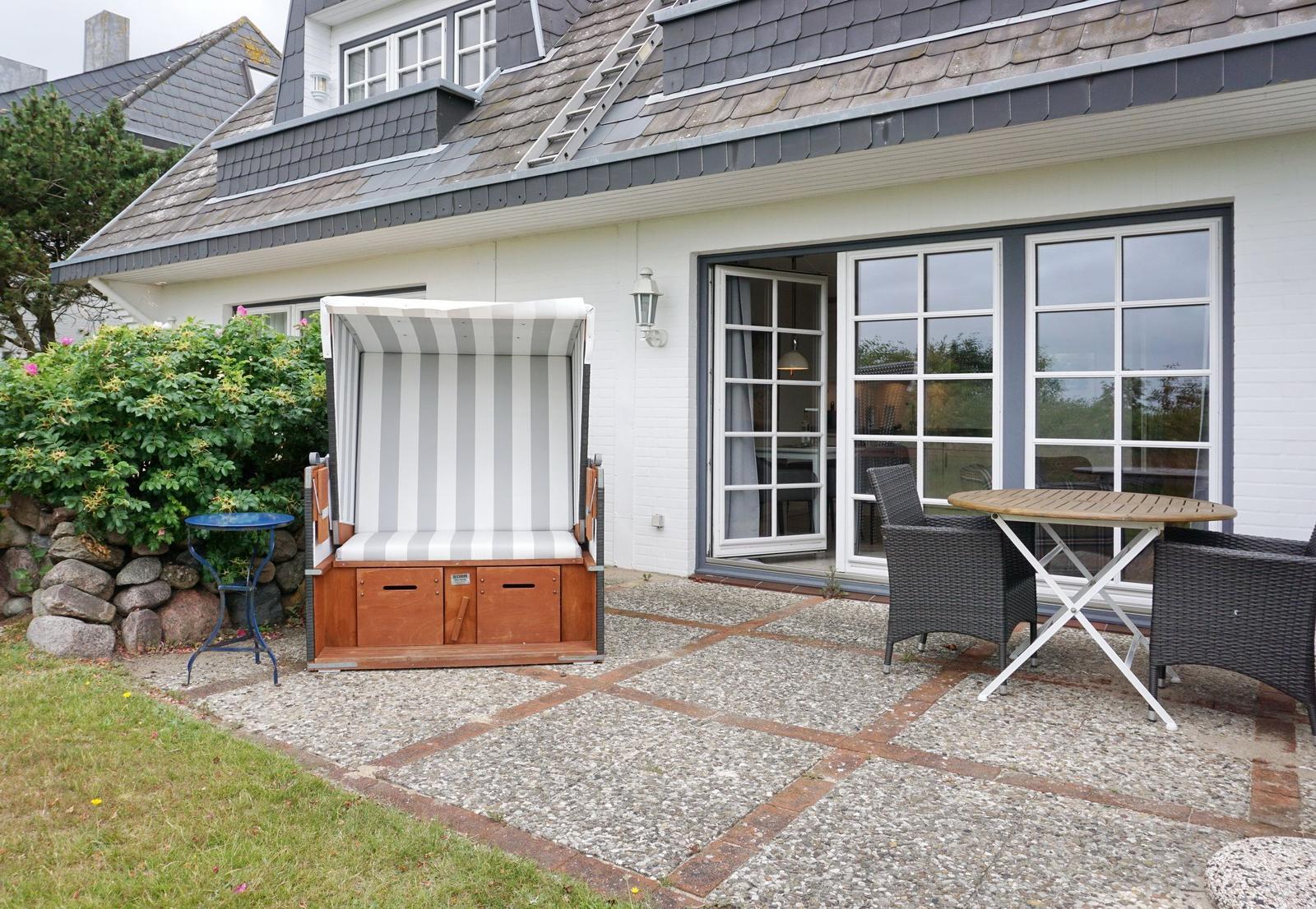 Terrace with beach chair, table and chairs in front of a house with sliding doors.