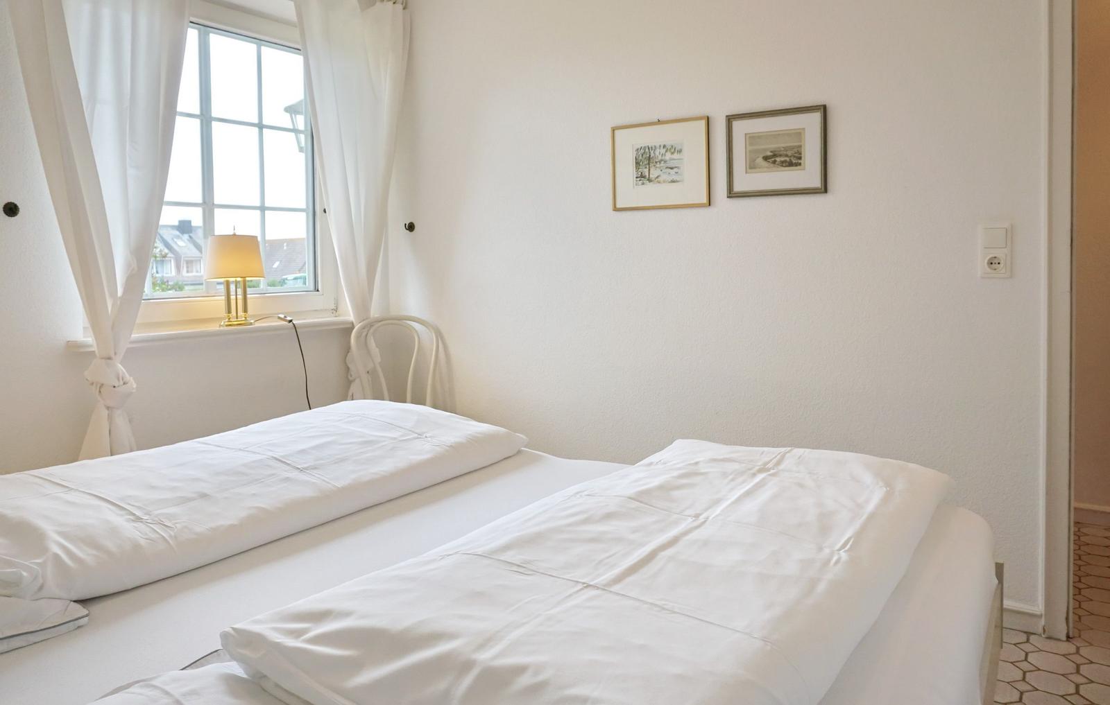 A bedroom with a white bed, window, and two pictures on the wall.