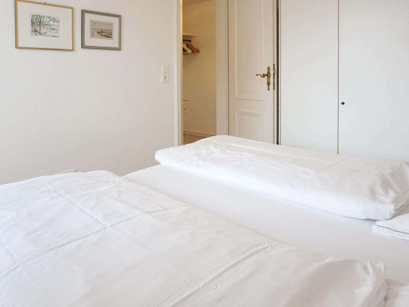 Bedroom with white bed, closet, and pictures on the wall.