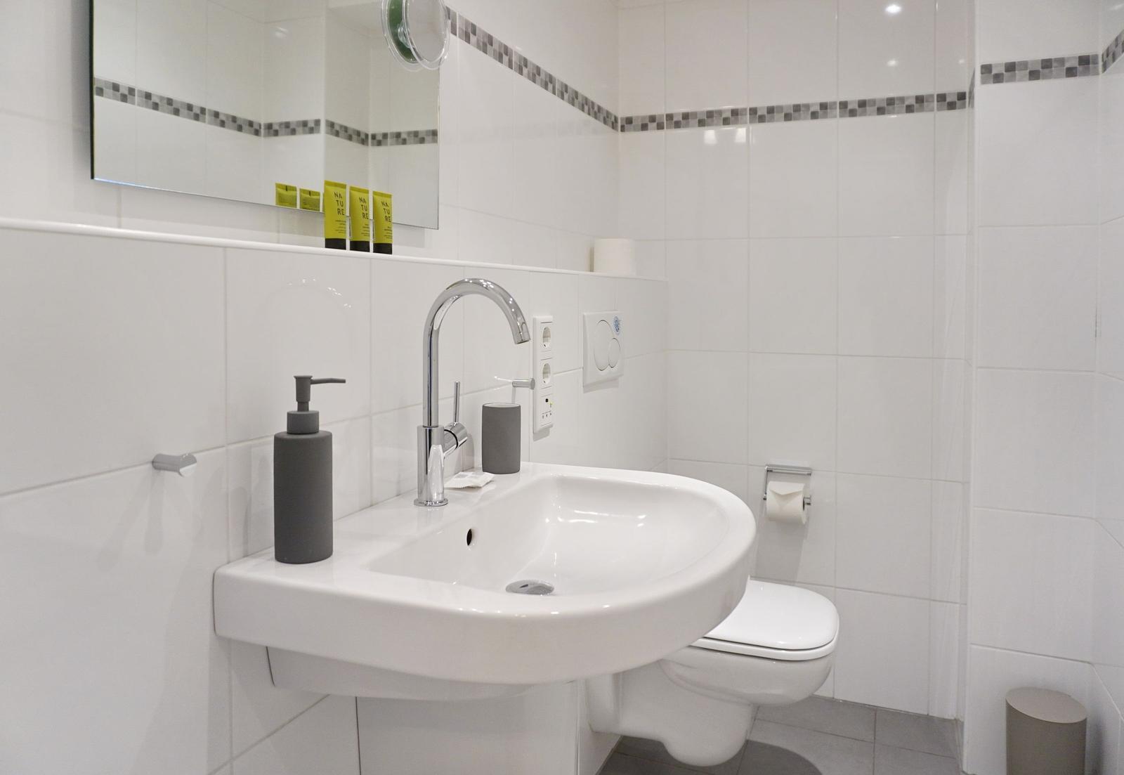 Bathroom with sink, mirror, and toilet. White tiles and gray accessories.