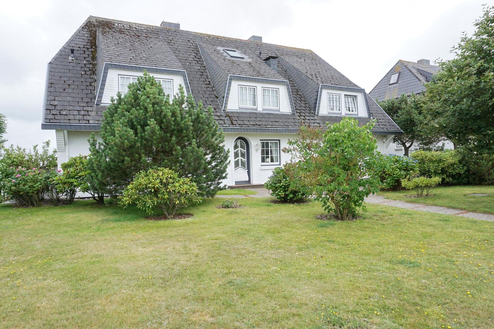 House with gray roof and white facade, surrounded by grass and trees.