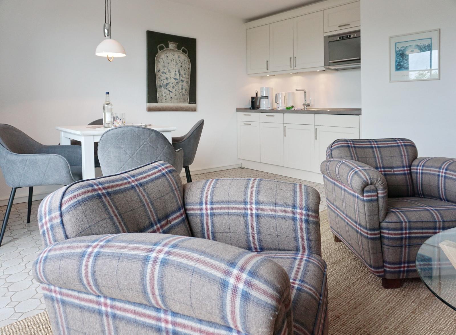 Two comfortable armchairs with checkered fabric, dining area and kitchen in background.