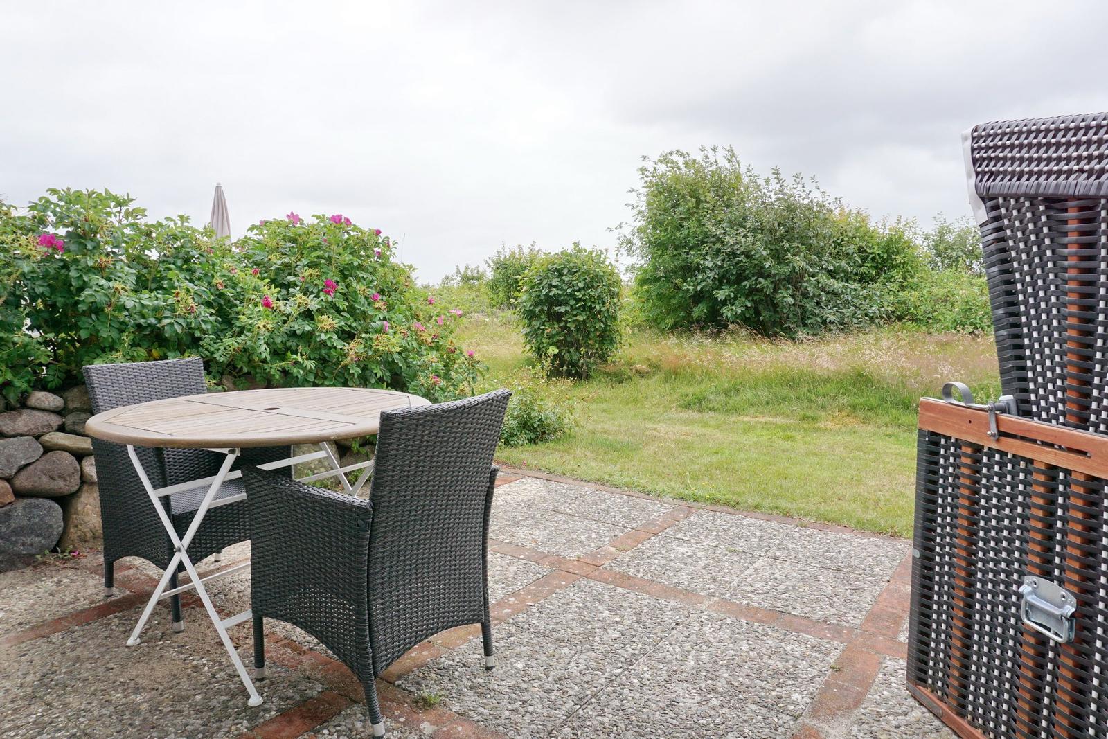 Terrace with table and chairs, surrounded by green areas and shrubs.