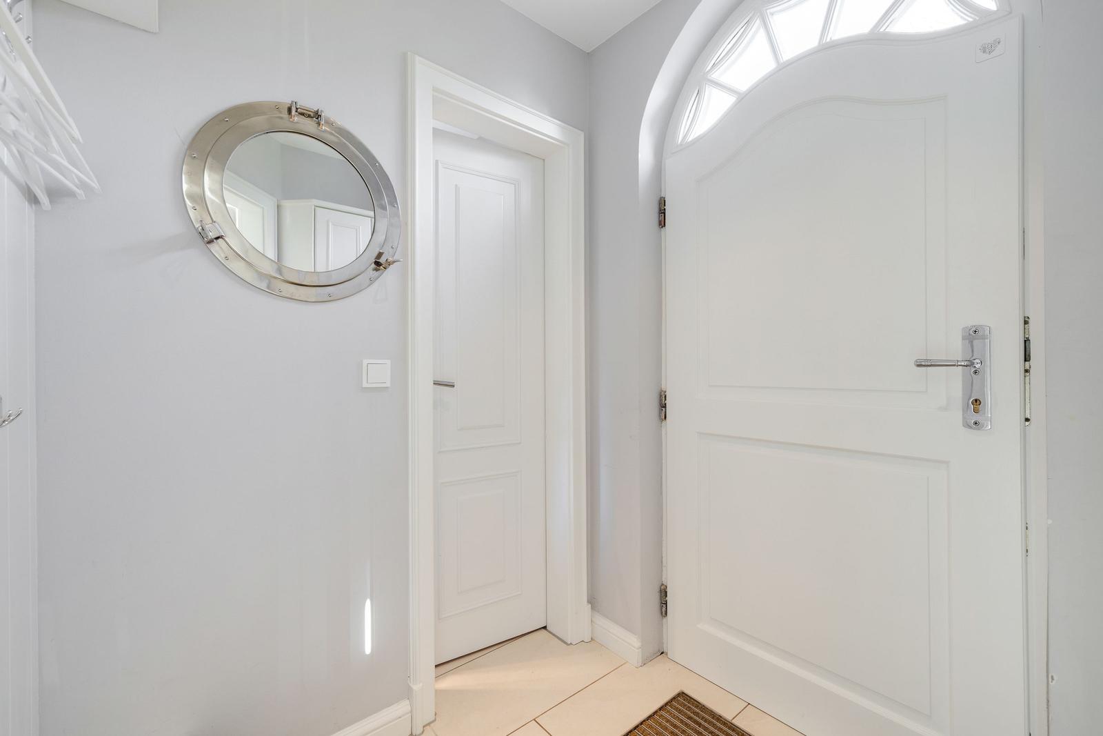 Entrance area with white door, round mirror, and tiled floor.