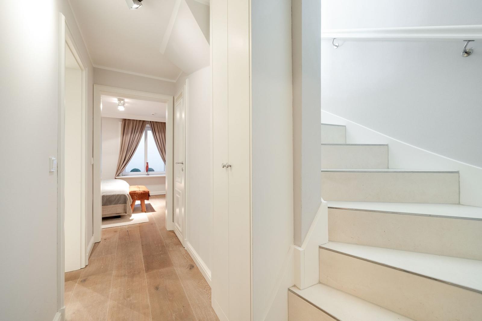 Hallway with stairs and view into bedroom with bed and window