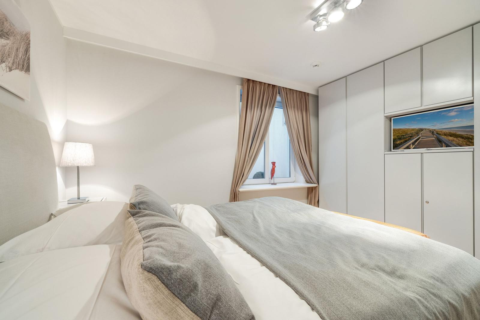 Bedroom with bed, nightstand, window, and wardrobe.