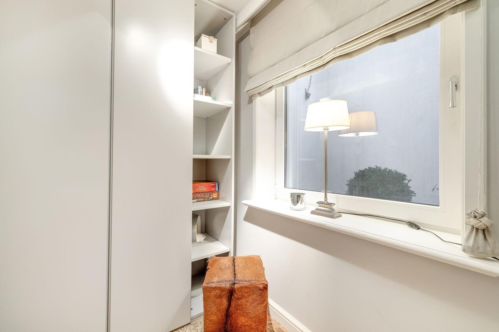 A room with a white wardrobe, a window, and a brown stool.