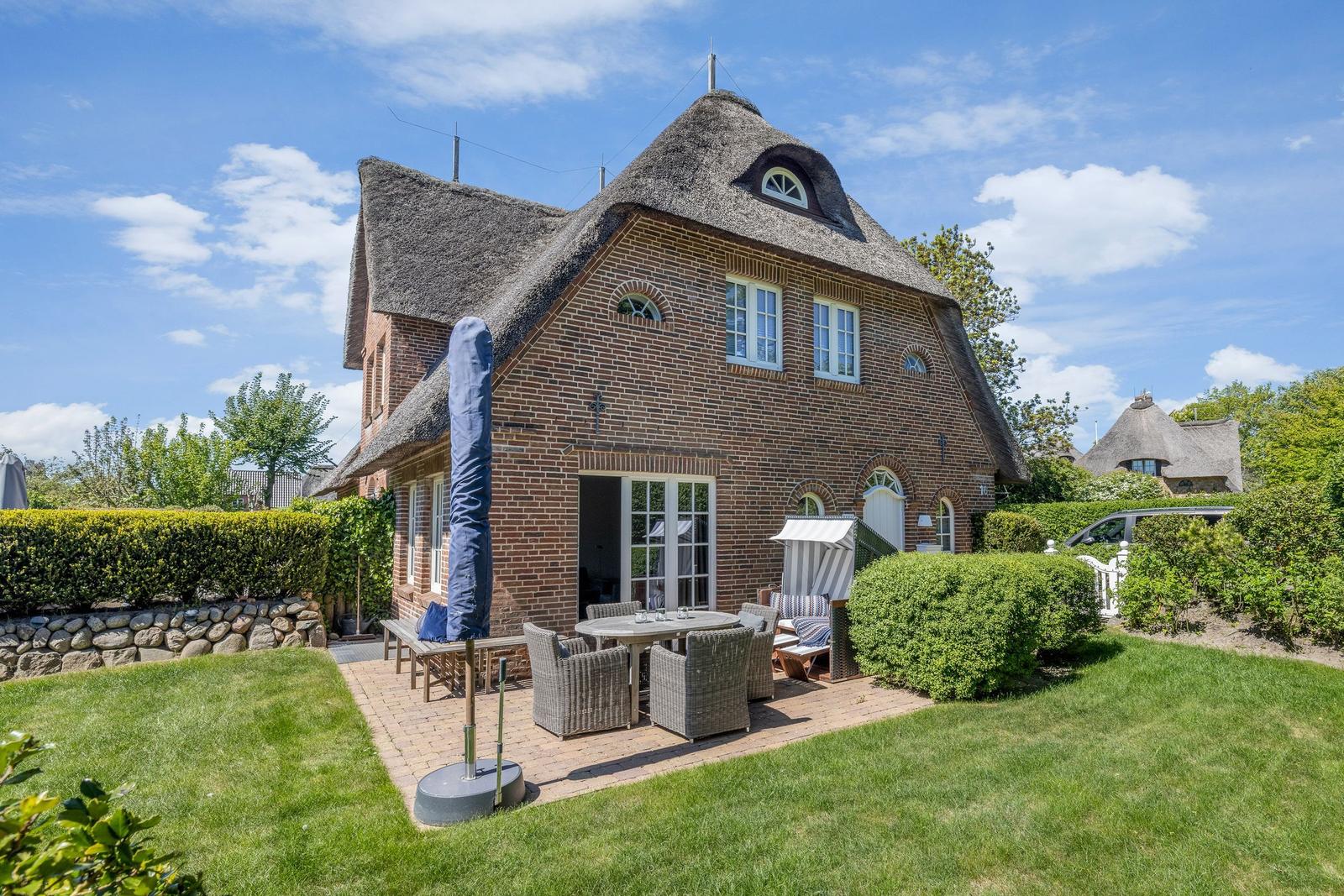 Red brick house with thatched roof and garden area with seating.