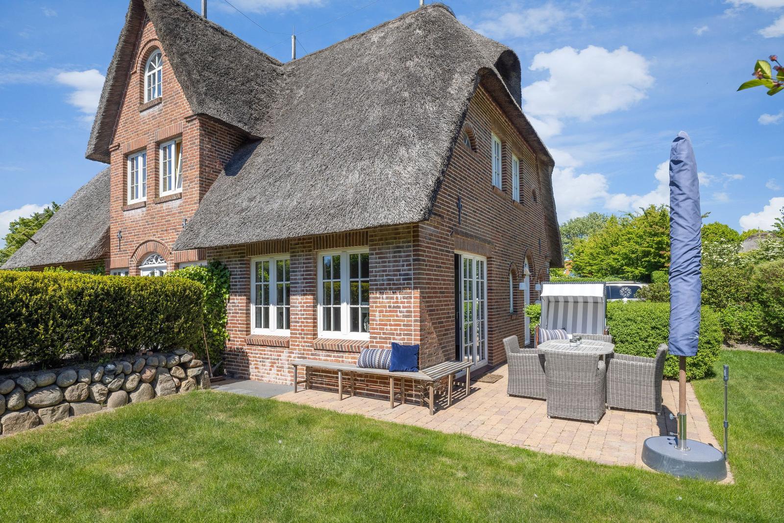 House with thatched roof, terrace with garden furniture and green lawn.