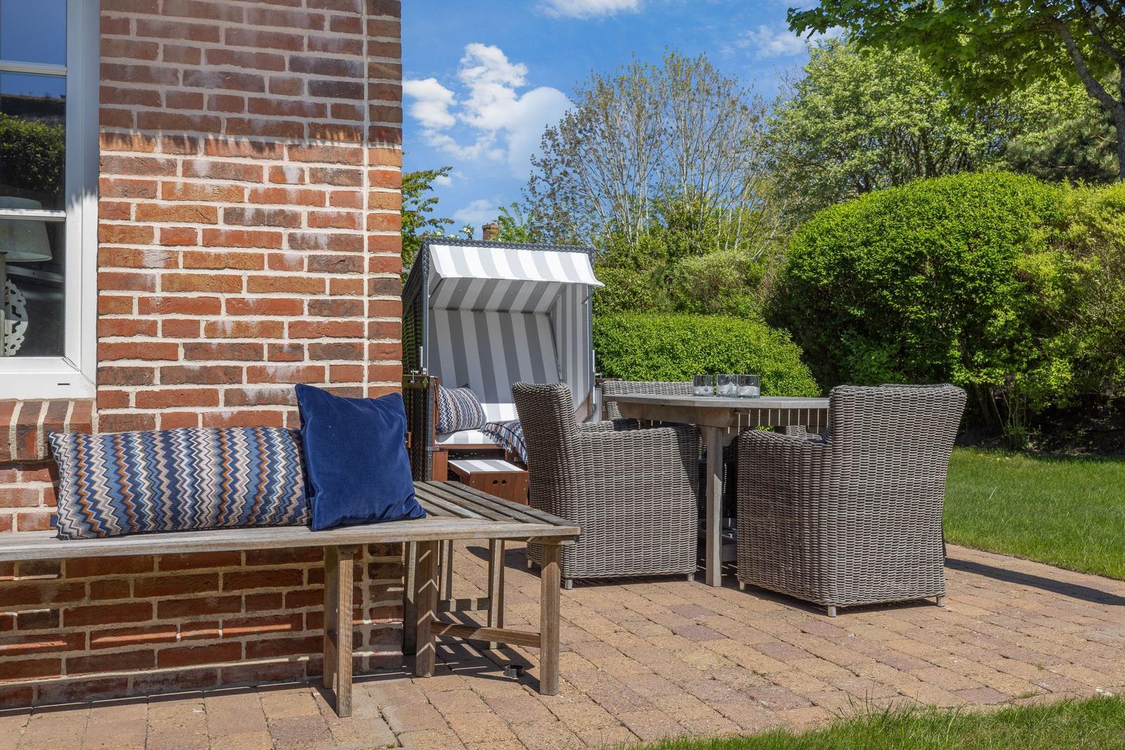 Terrace with seating and beach chair. Background: greenery and blue sky.