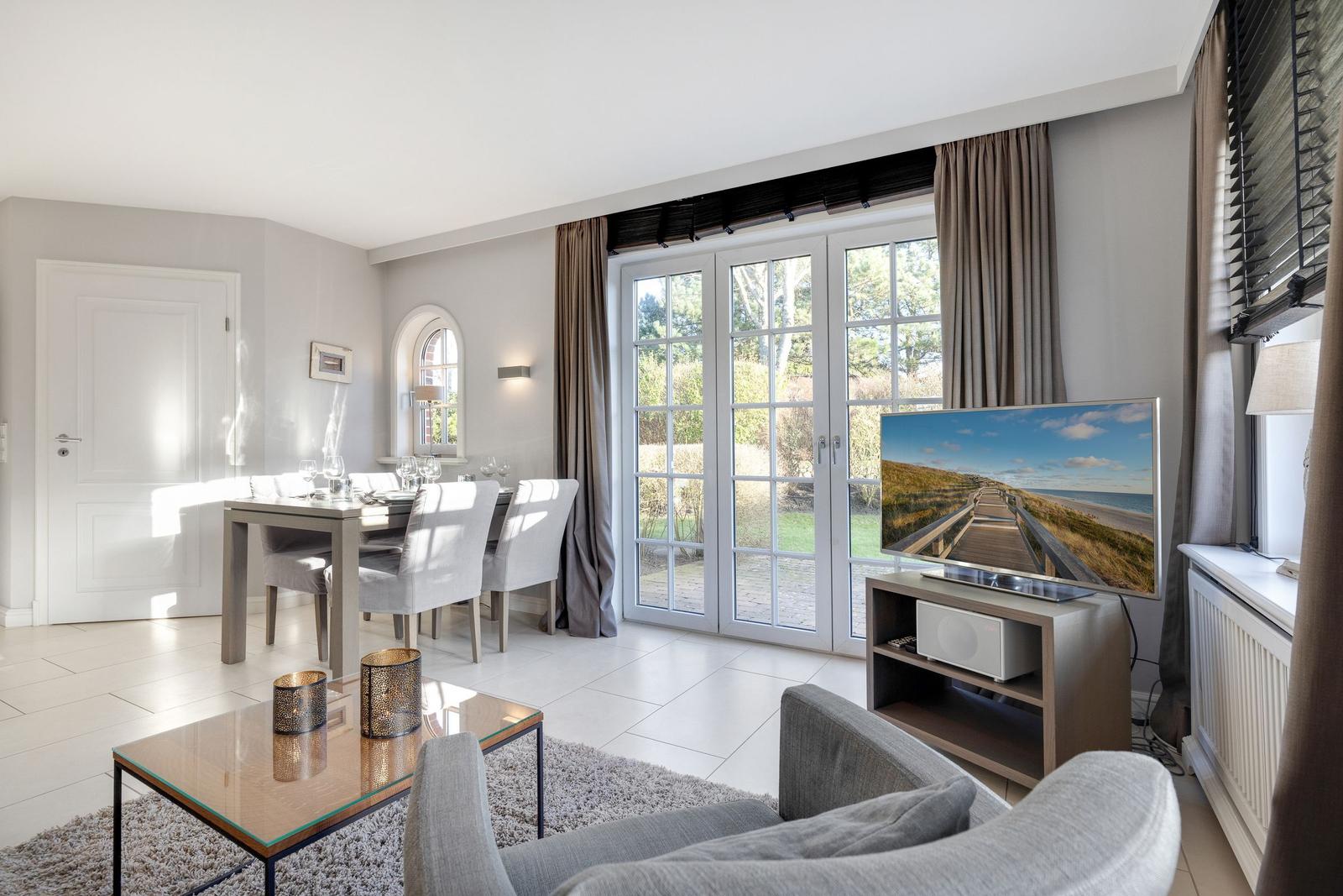 Living and dining area with TV, table, chairs, and windows to the garden.