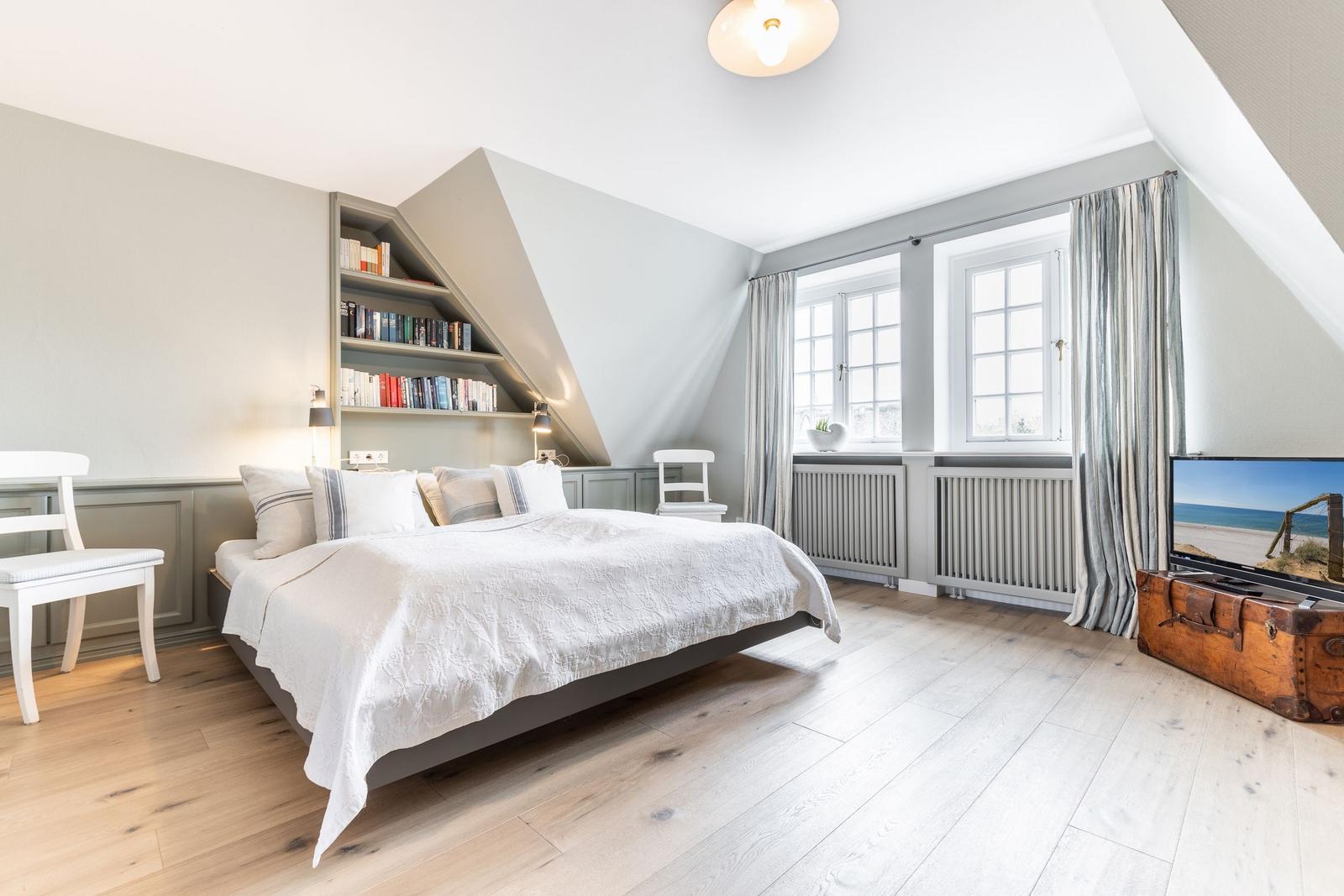 Schlafzimmer mit Dachschrägen, Bücherregal, Fenstern und Holzboden.