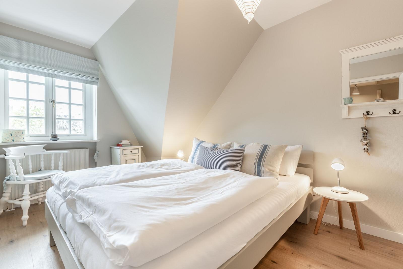 Schlafzimmer mit Dachschräge, Bett, Fenster und Nachttisch.