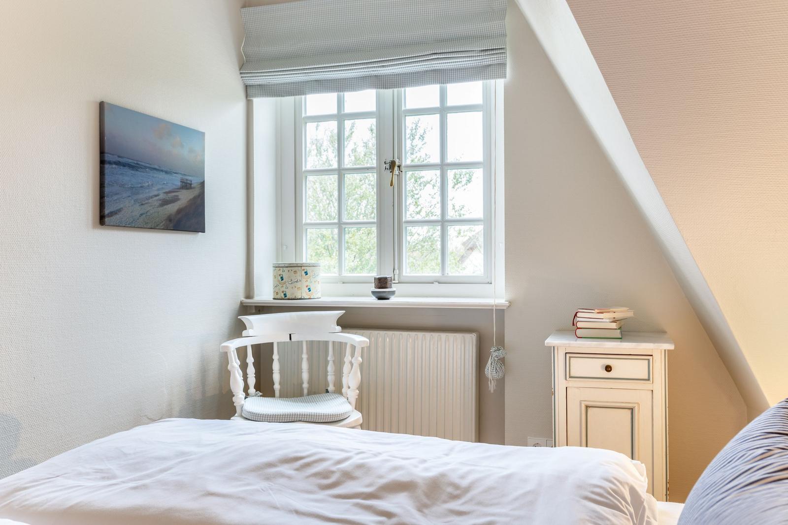 Schlafzimmer mit Dachschräge, Fenster, Stuhl und Nachttisch.