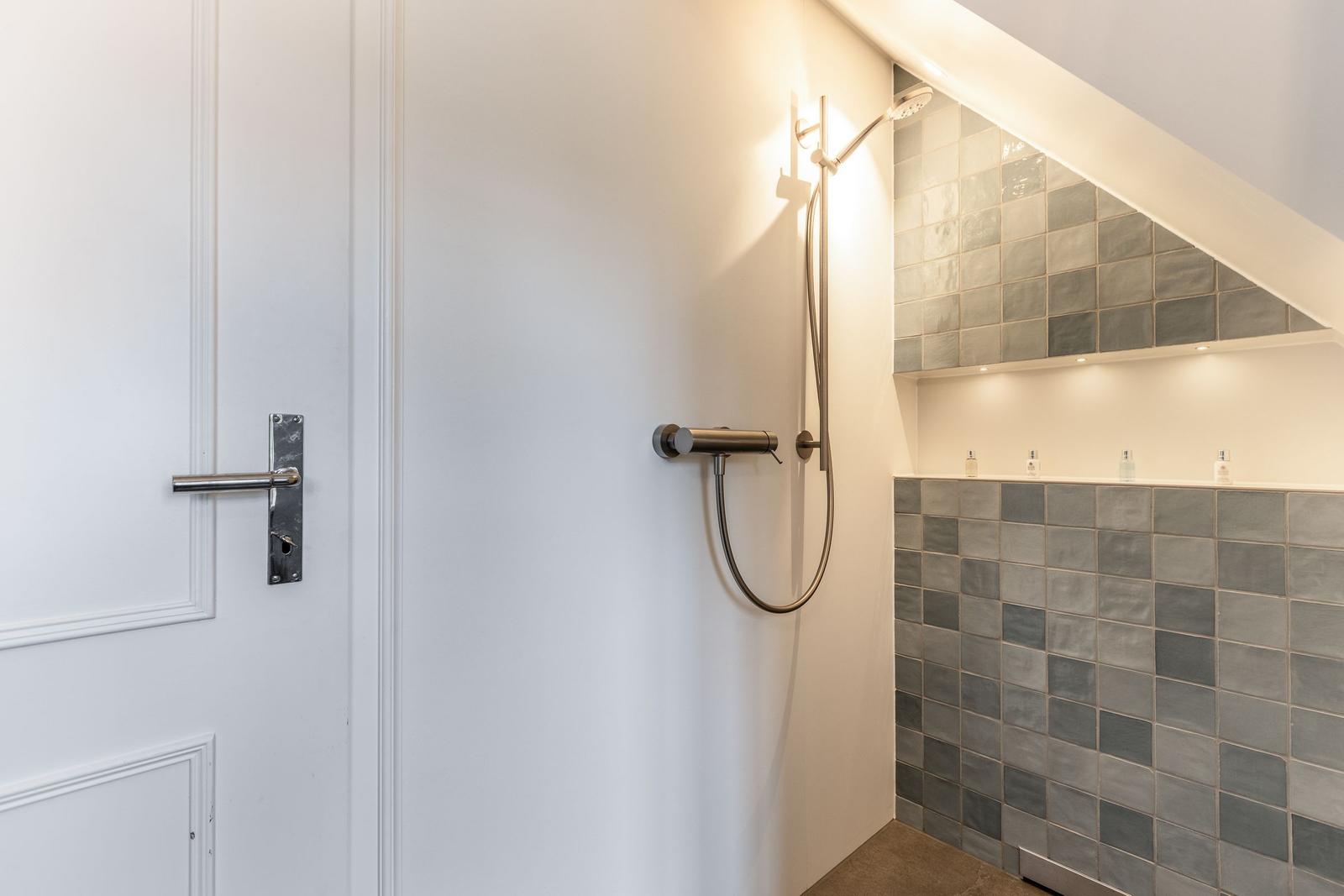 Dusche mit Duschbrause und grauen Fliesen an der Wand