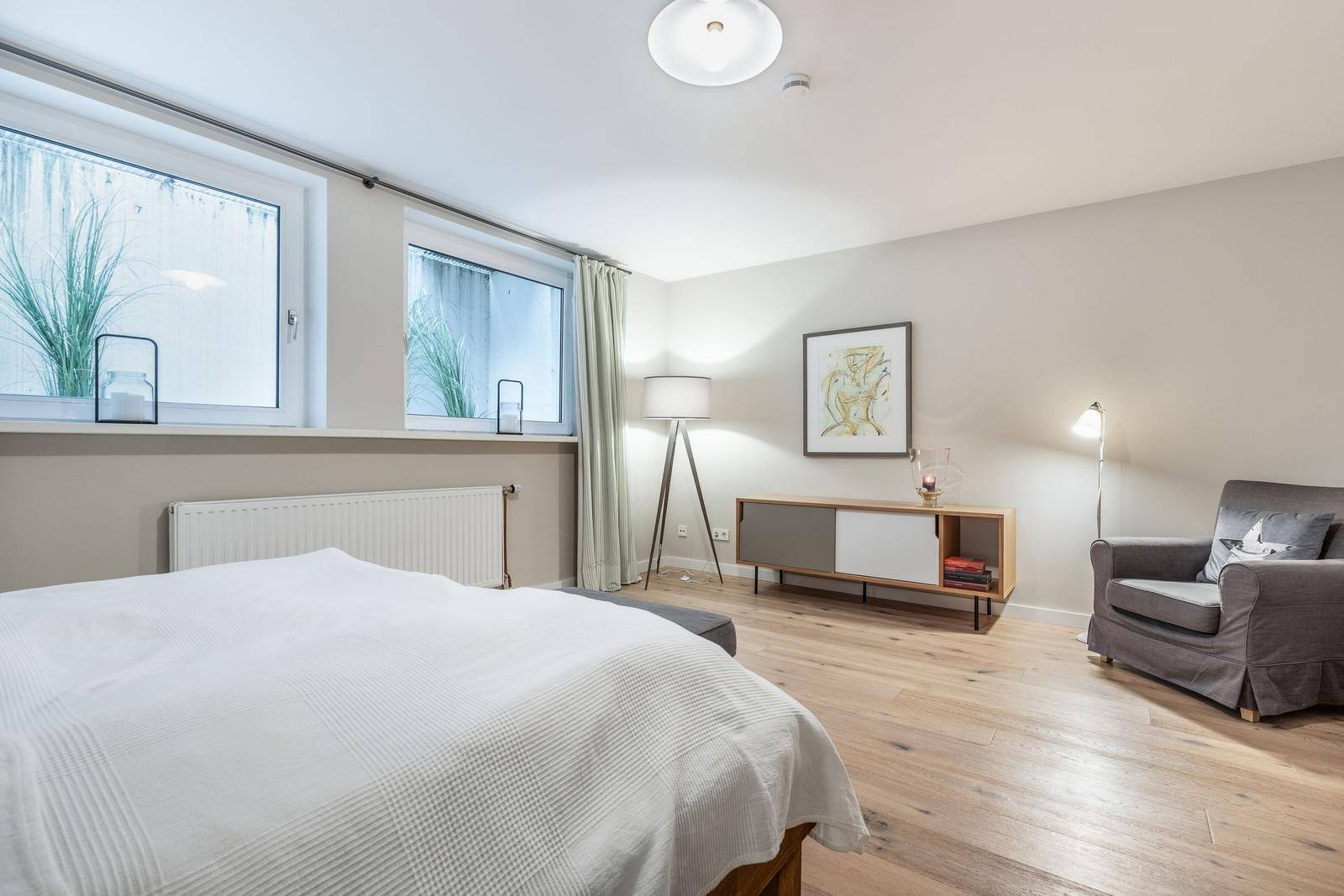 Schlafzimmer mit Bett, Sessel und Fenstern.