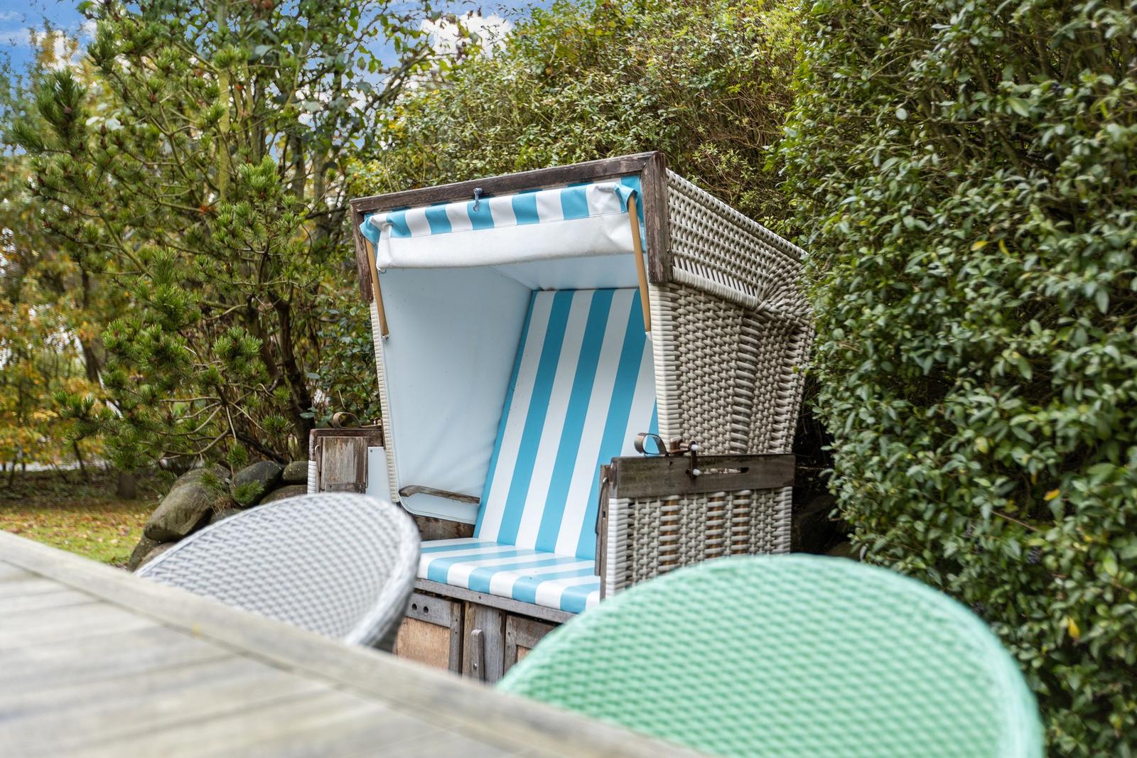 Strandkorb mit blau-weißem Stoff und geflochtenem Rahmen im Garten.