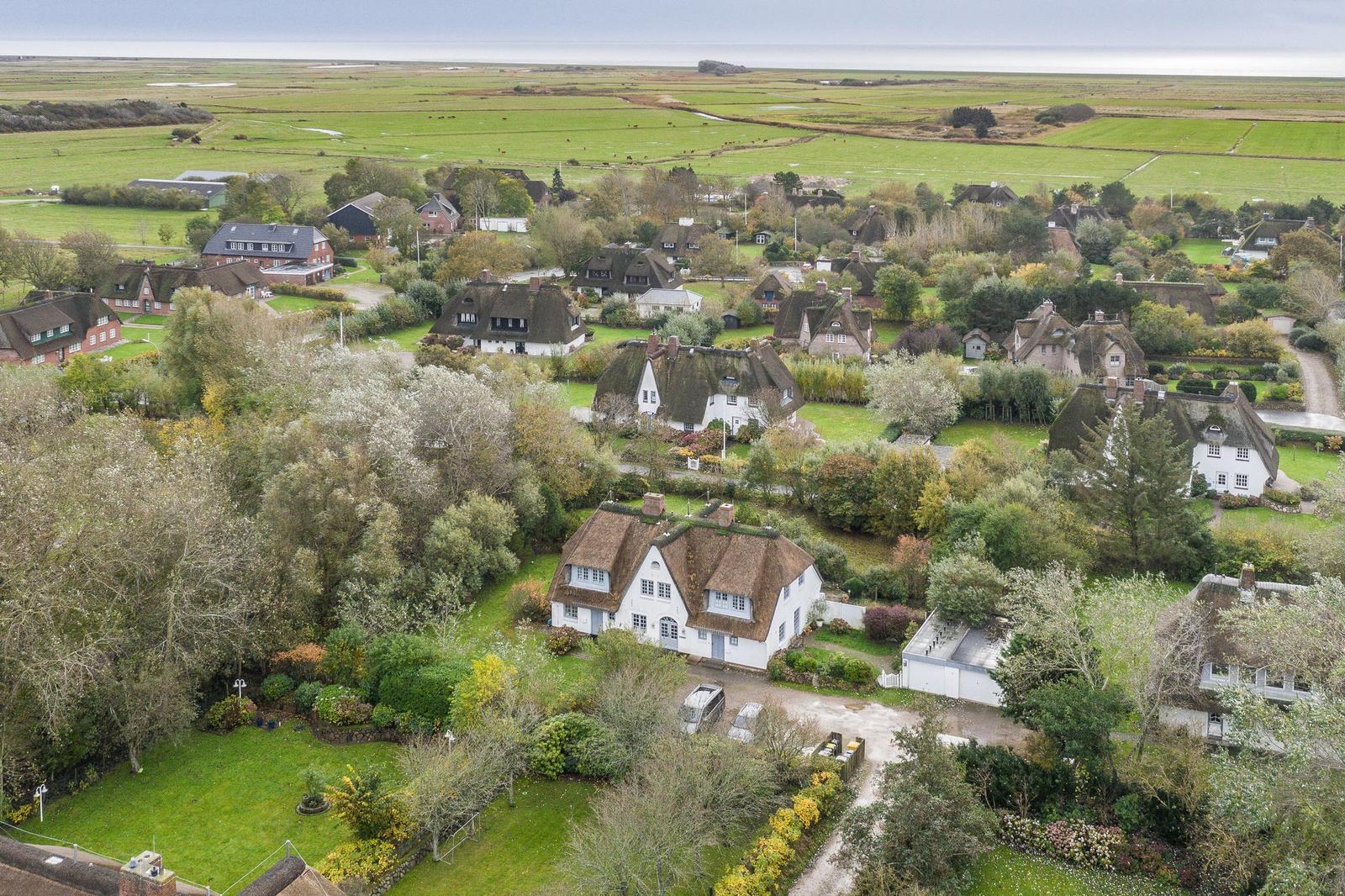 Dorf mit strohgedeckten Häusern und grünen Wiesen im Hintergrund.