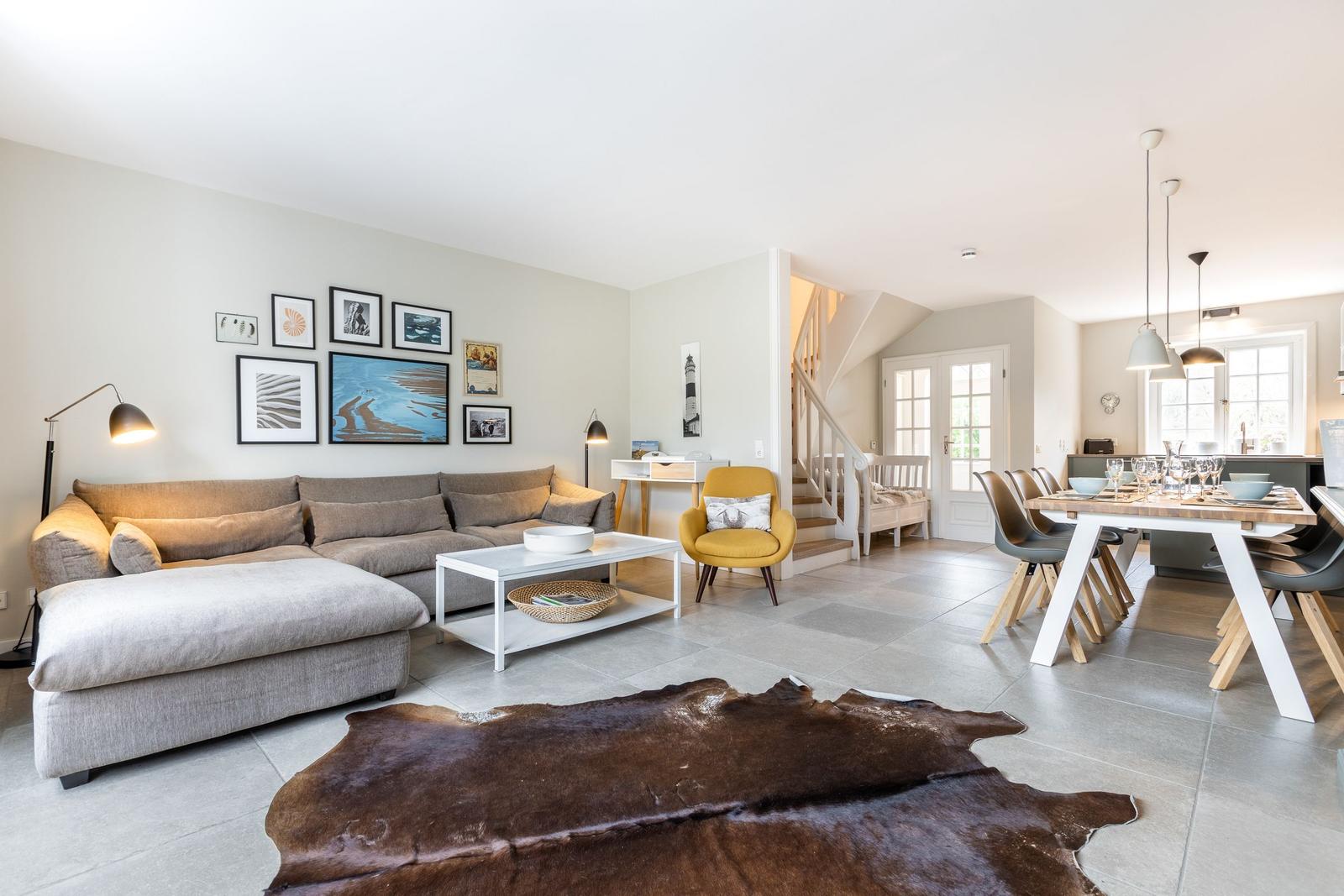 Wohn- und Essbereich mit Sofa, Tisch und Stühlen. Holzfußboden und Wandbildergalerie.