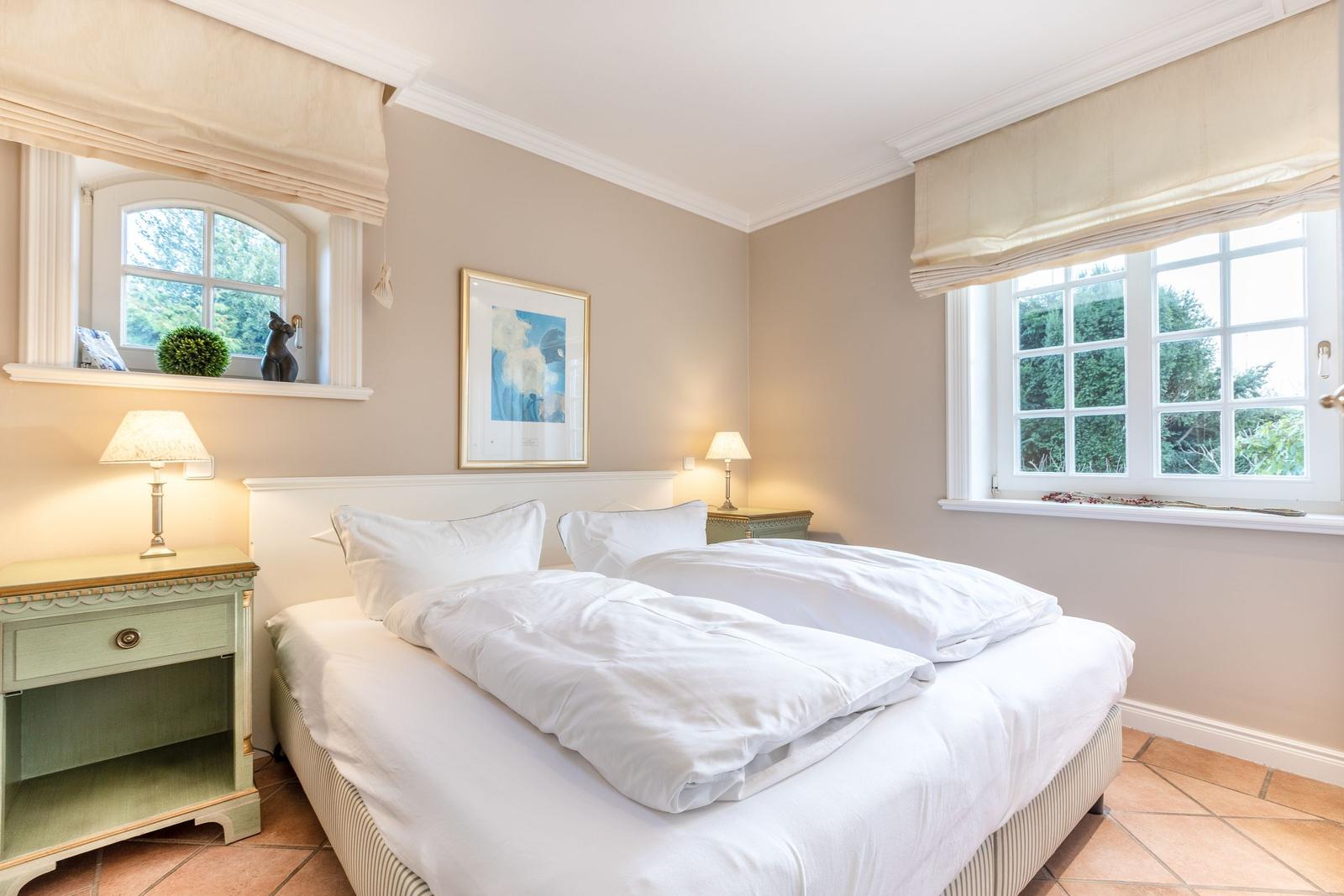 Bedroom with bed, two nightstands, and windows overlooking greenery.