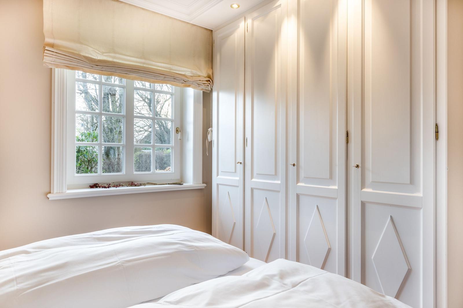 Bedroom with white bed, window, and white wardrobe doors.