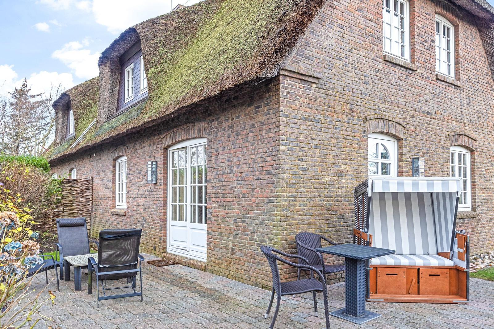 House with thatched roof and stone wall, outdoor area with table, chairs, and beach chair.