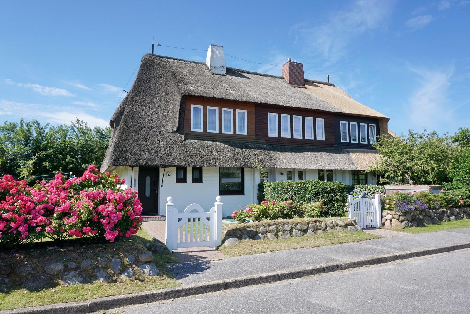 House with thatched roof, white window frames, and blooming rose bushes.