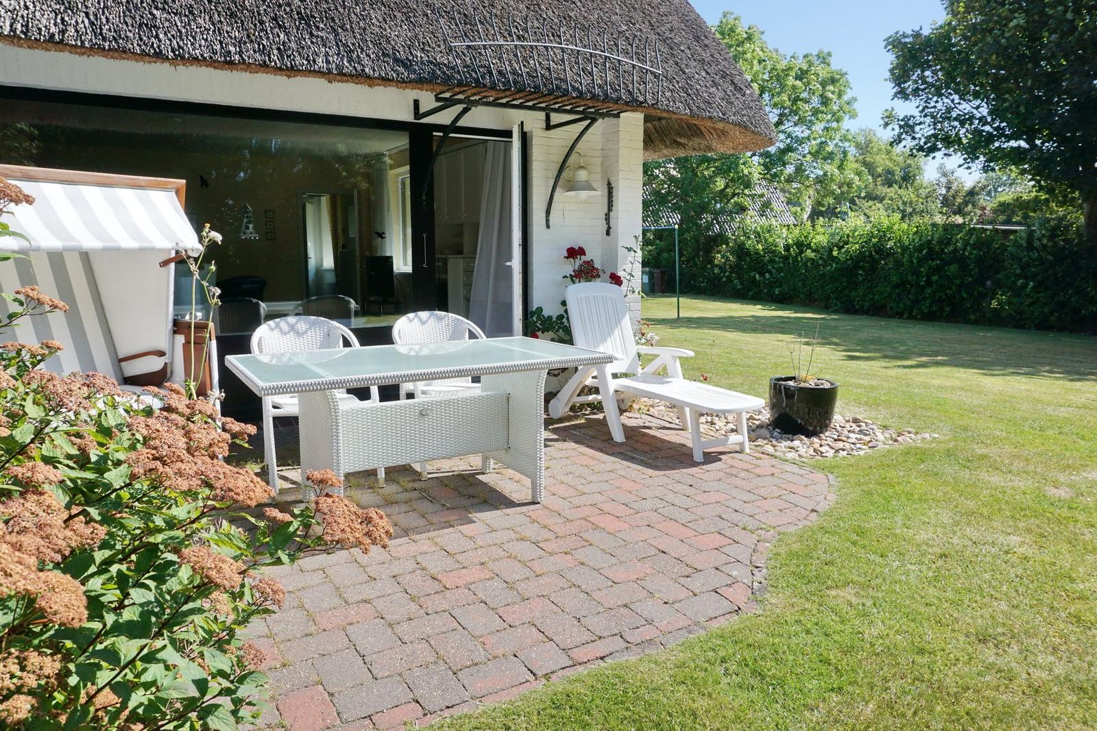 Terrace with white garden furniture and lawn in front of a house with thatched roof.