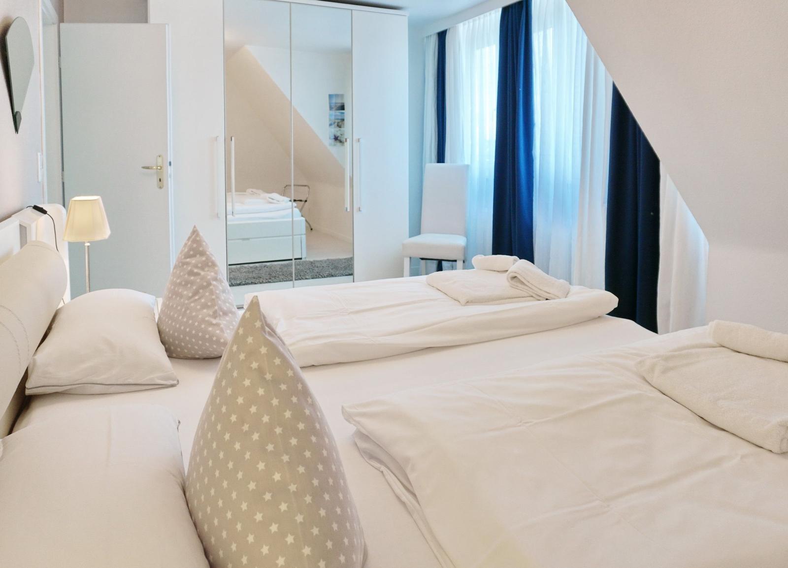 Bedroom with two beds, mirrored wardrobe, and window with curtains.