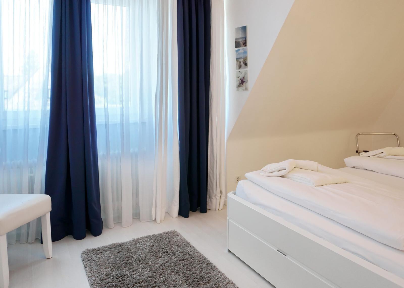 Bedroom with white bed, blue and white curtains, and gray rug.