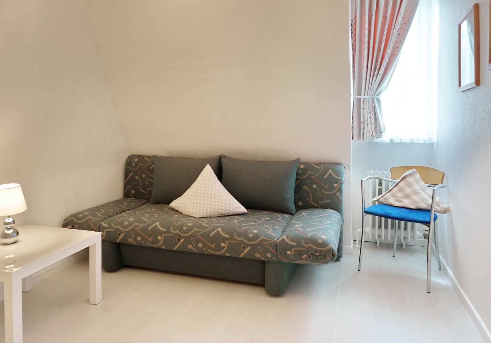 A room with sofa, table, chair and window with curtains.