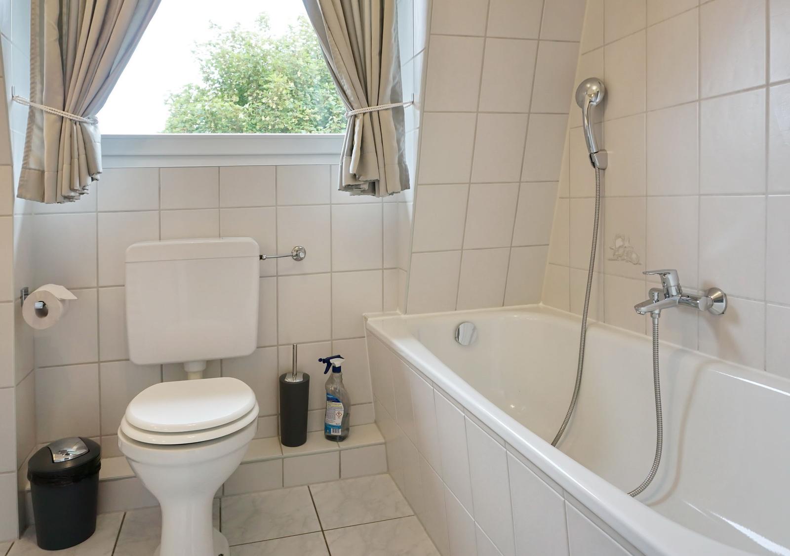 Bathroom with bathtub, toilet, and window with curtains.