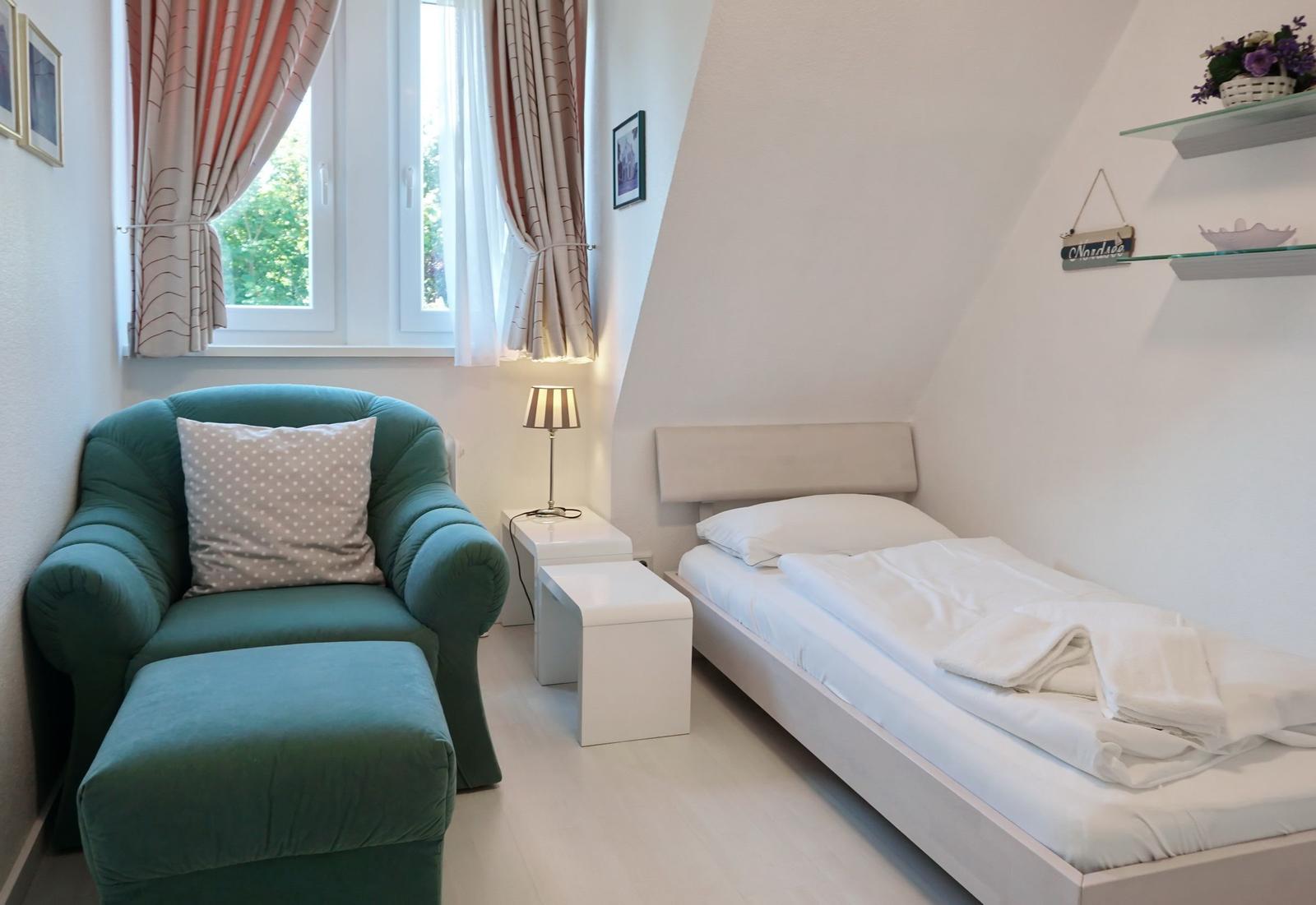 Bedroom with bed, green armchair, and window with curtains.