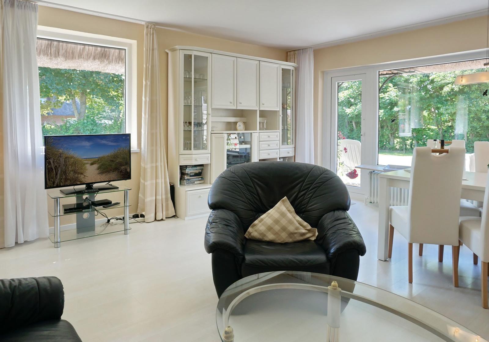Living room with dining area, black leather armchair, and TV. View of garden.