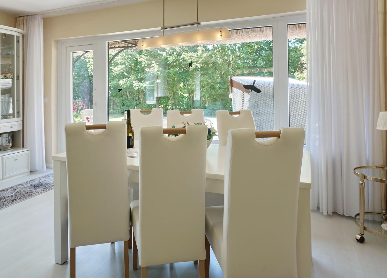 Dining room with white table and chairs, large window overlooking garden.