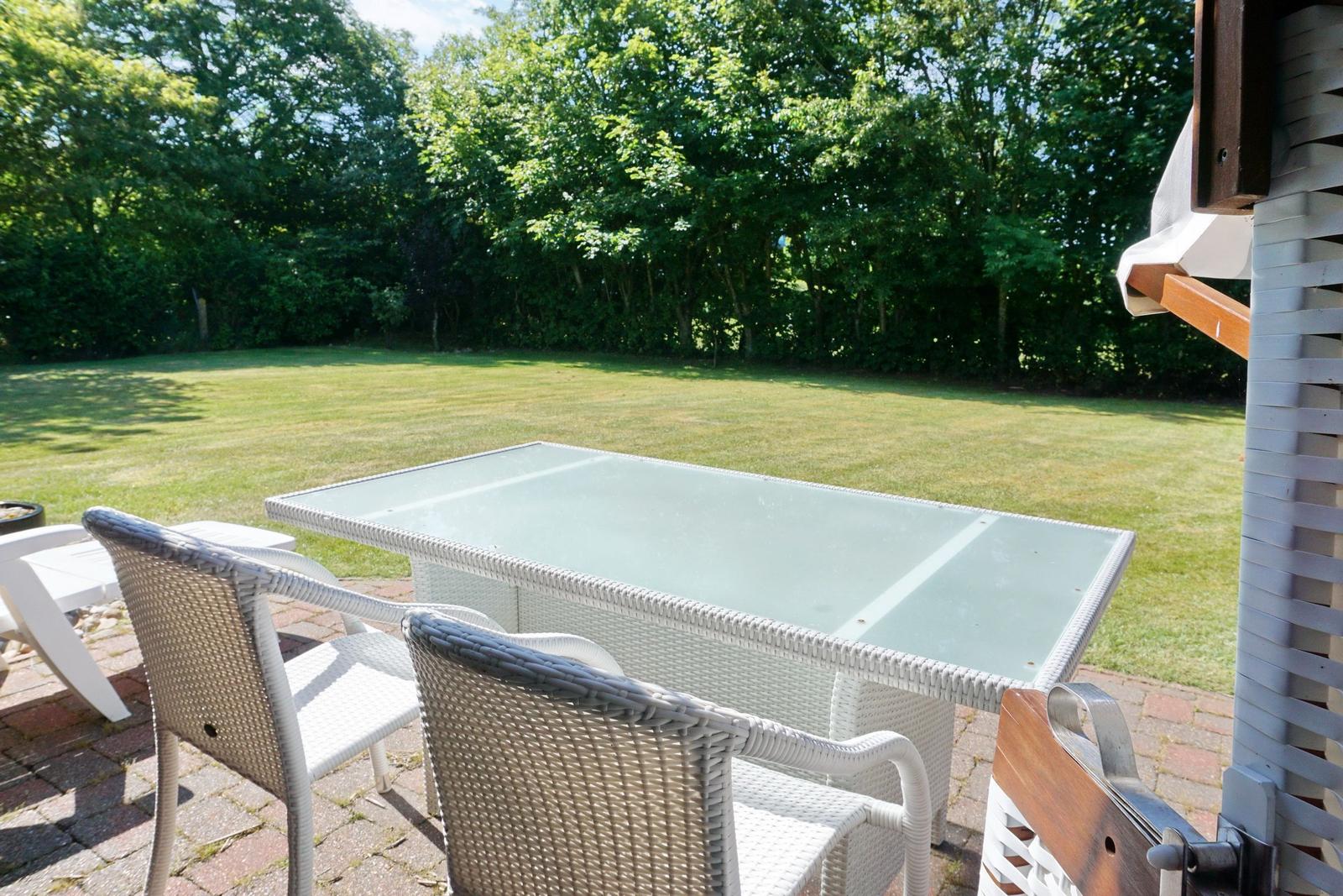 Terrace with table and chairs, view of green lawn and trees.