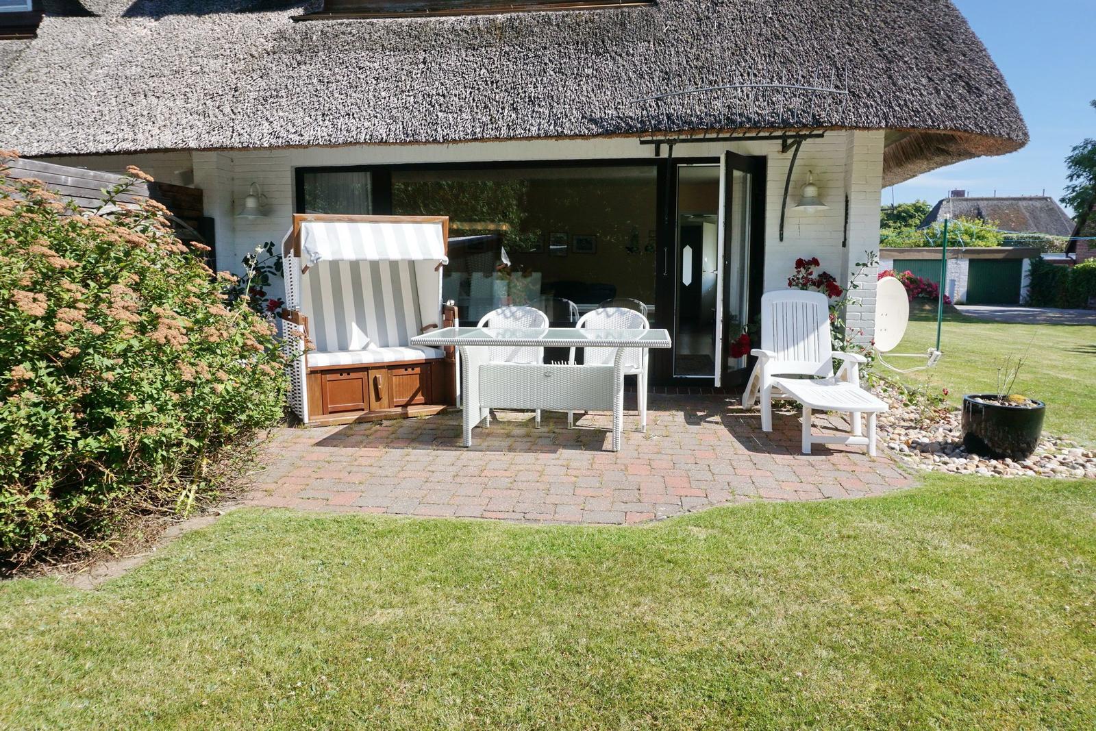 House with thatched roof and terrace with garden furniture.
