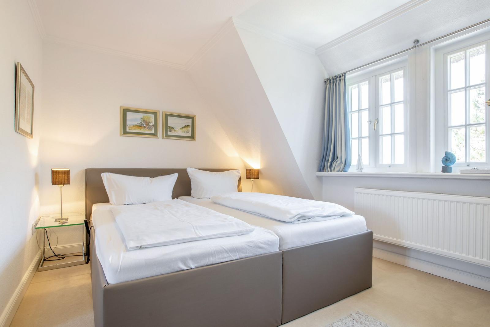 Schlafzimmer mit Doppelbett, Fenstern und Wandbildern.