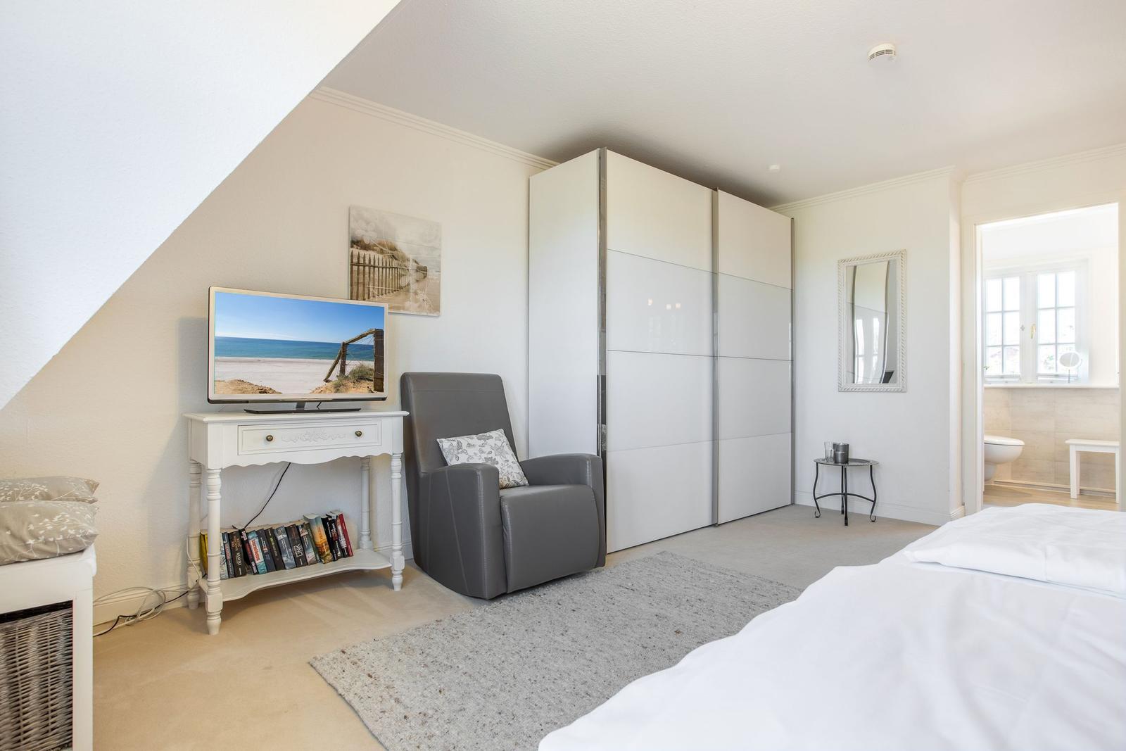 Schlafzimmer mit Bett, Kleiderschrank, Sessel und Fernseher.