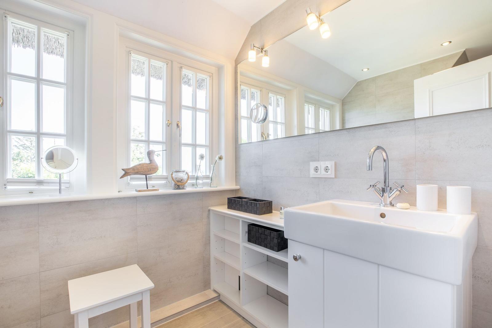 Badezimmer mit Waschbecken, Spiegel und Fenstern.
