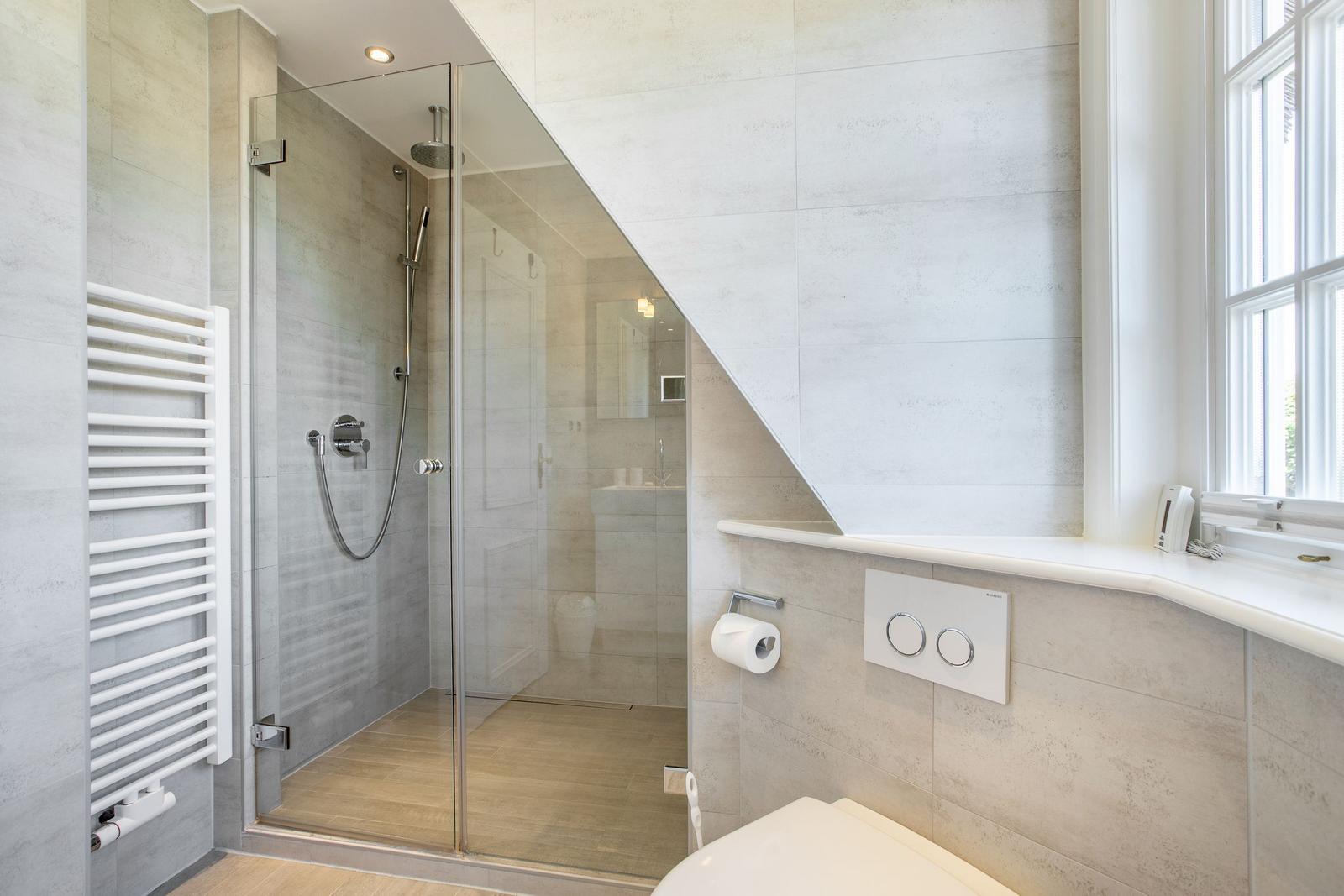 Dusche mit Glaswand, Toilette und Fenster im Badezimmer.