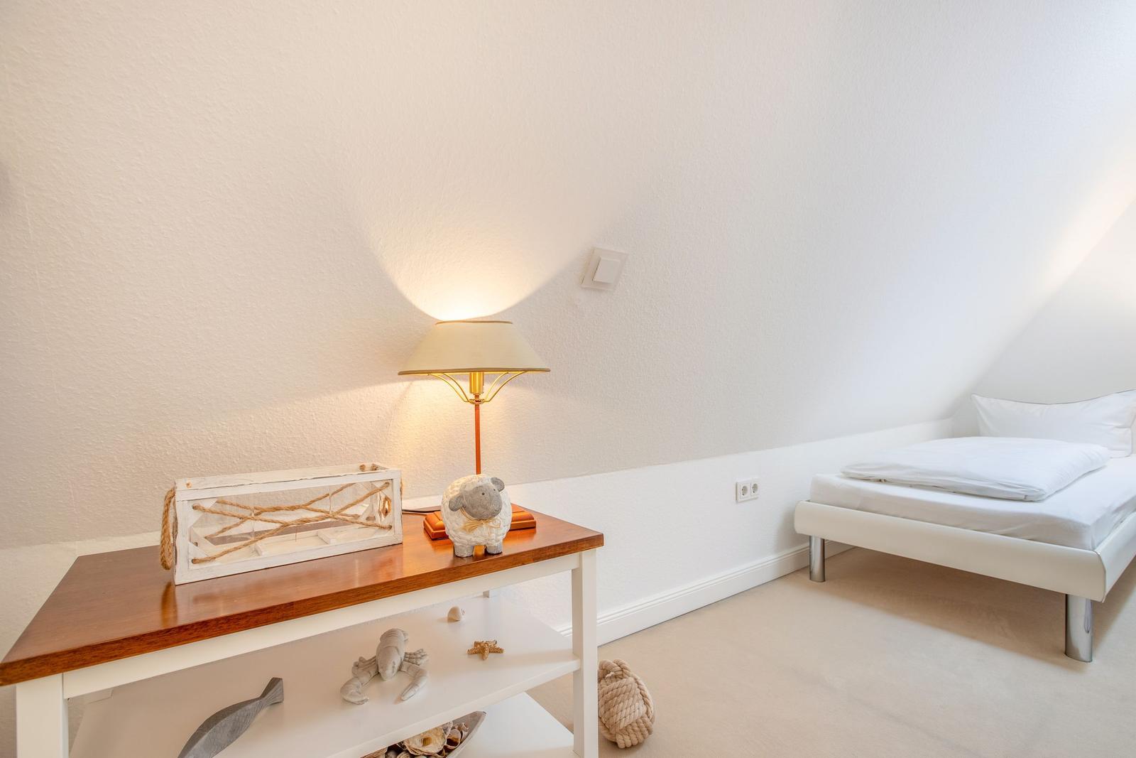 Schlafzimmer mit weißem Bett und Holztisch mit Lampen und Dekoration.