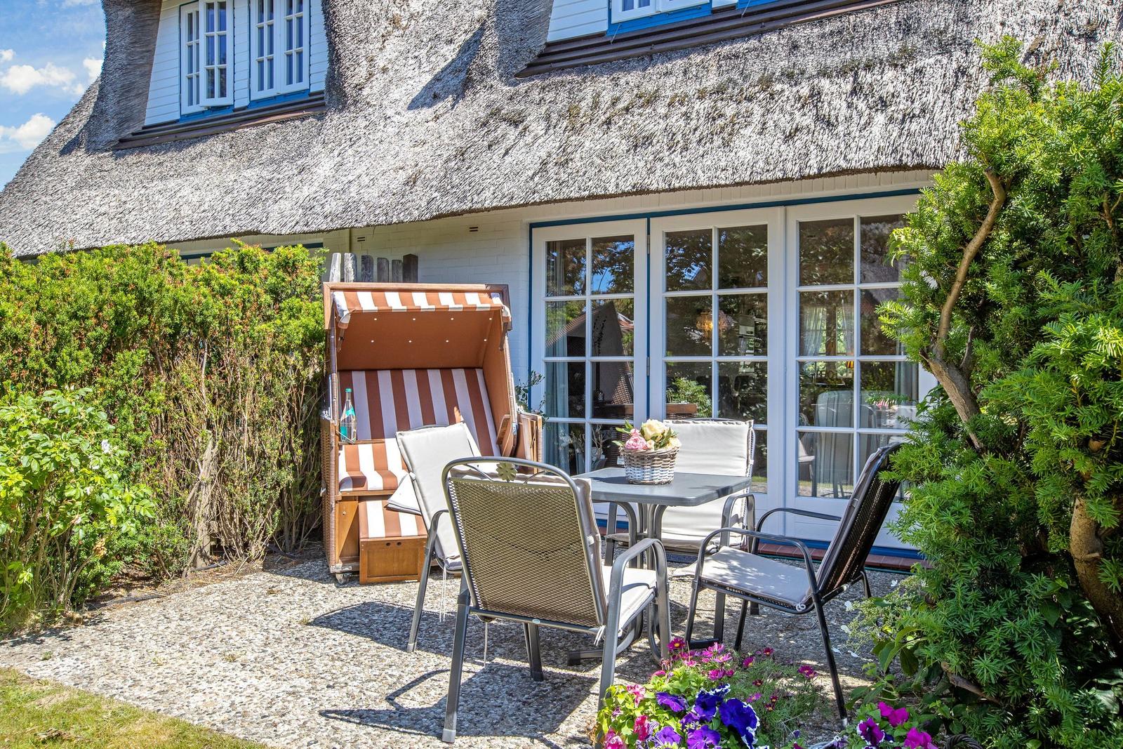 Haus mit Strohdach, Terrasse mit Tisch, Stühlen und Strandkorb.
