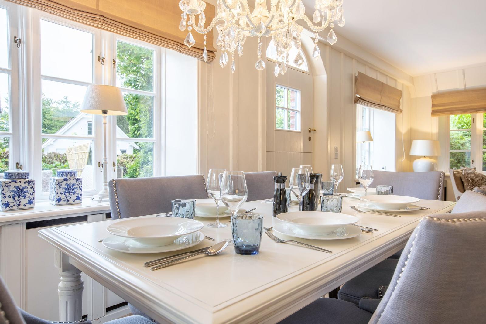 Dining room with set table, chandelier, and windows to the garden.