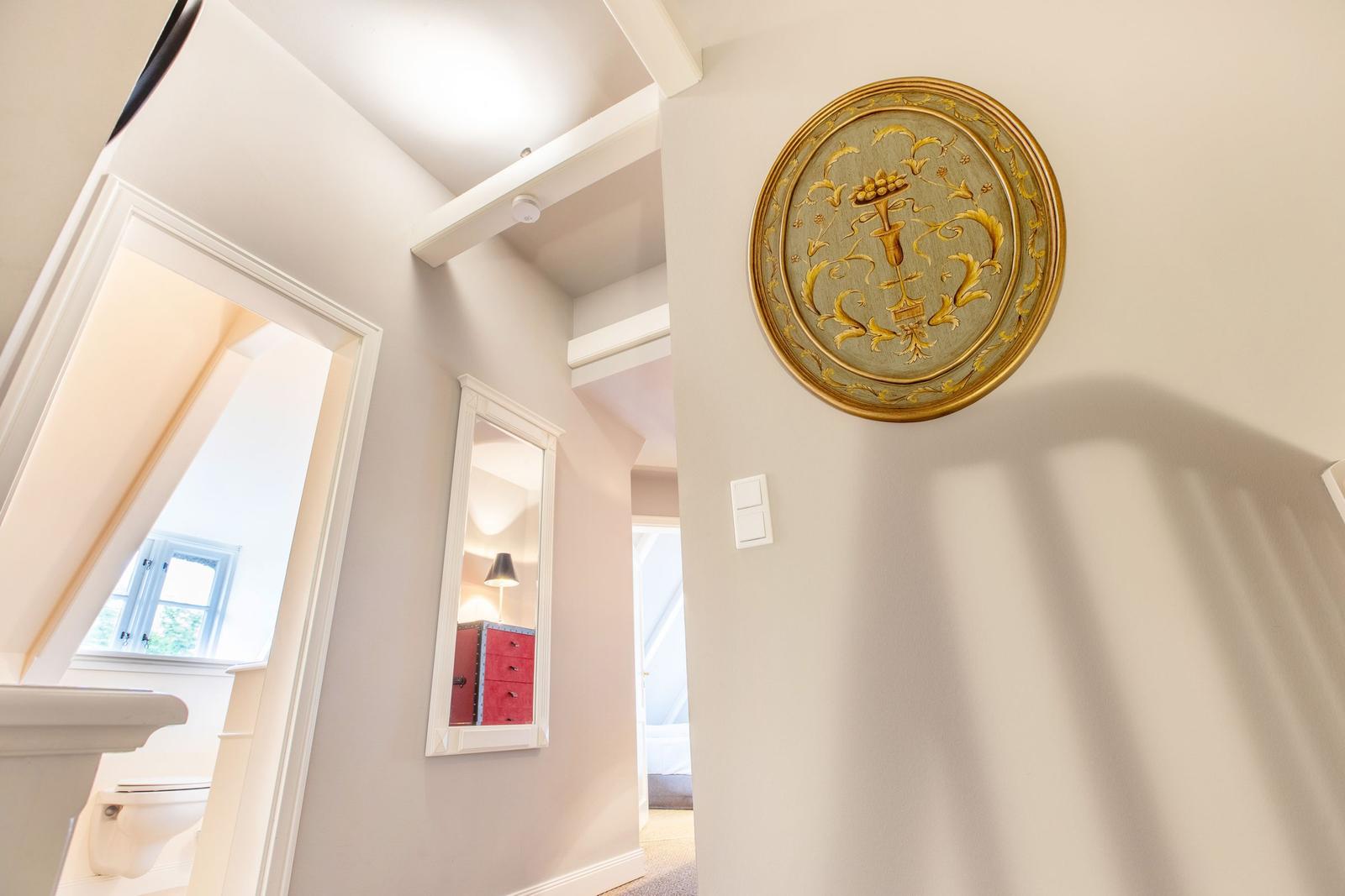 Hallway with gold-framed wall art, mirror, and doorways to bedroom and bathroom.