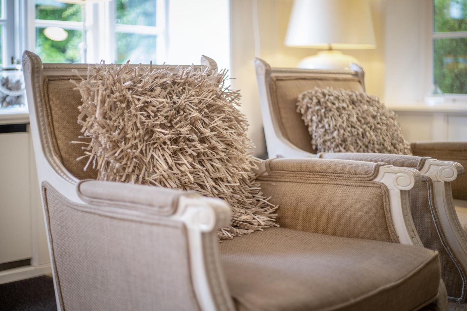 Two chairs with straw cushions and white wooden frames stand by a window.
