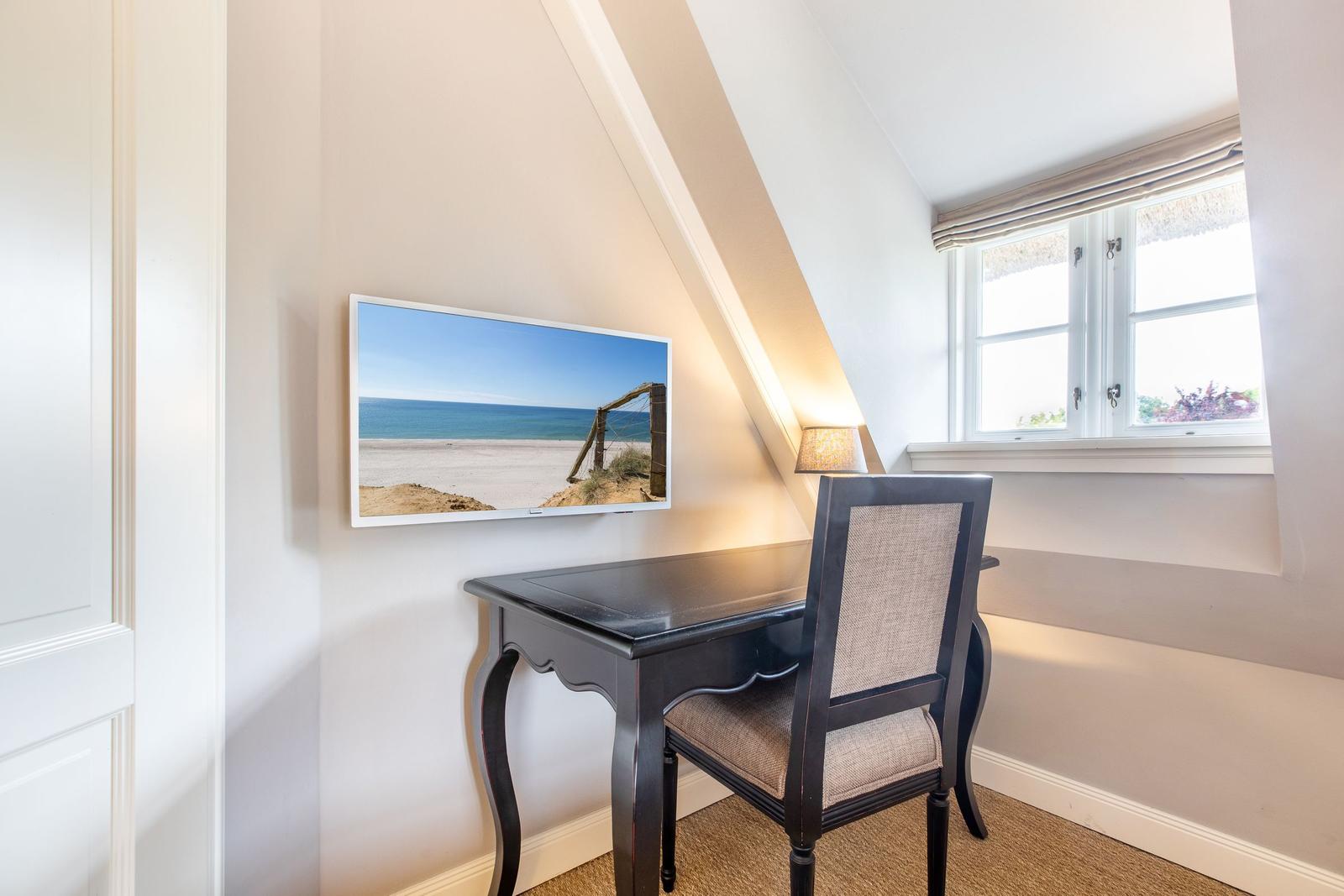 Desk with chair under sloped ceiling and window. Wall picture shows beach.